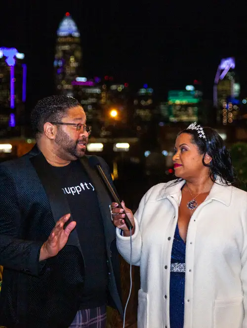 african american woman interviewing african american man outdoors at night with city skyline in background