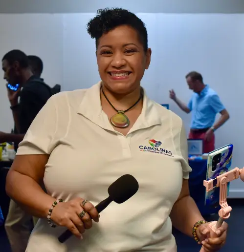 mel morris african american woman in white shirt with logo holding a microphone and cell phone on a selfie stick, smiling